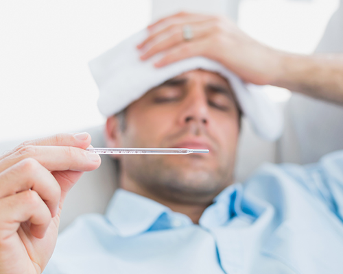 Man with a wet towel over the head looking at thermometer experiencing a fever