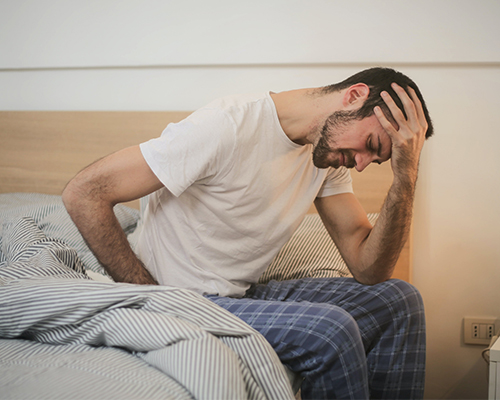 Man sitting on bed clutching his stomach in pain